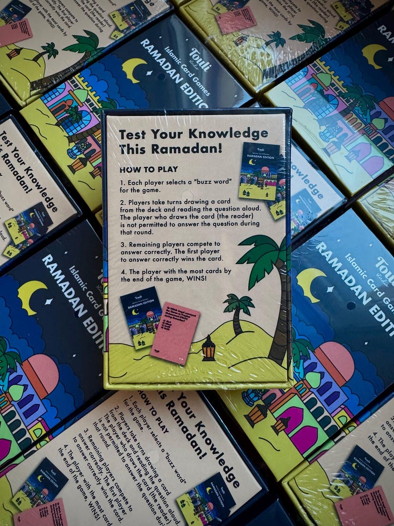 May include: A yellow box with a colorful illustration of a mosque and palm trees. The box contains a card game called "Test Your Knowledge This Ramadan!" with instructions on how to play. The game is designed to test players' knowledge about Ramadan.