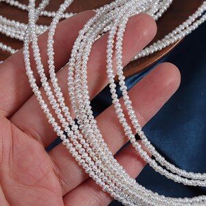 May include: Close-up of multiple strands of small, white pearls. The pearls are strung together, creating a delicate and elegant appearance. The pearls are held in a hand, with a blue background.