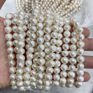 May include: A strand of white freshwater pearls, each pearl is round and smooth. The pearls are strung on a white thread and are ready to be used for jewellery making.