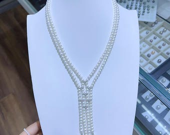 May include: A multi-strand pearl necklace displayed on a white bust. The necklace features three strands of small, round, white pearls that cascade down into a Y-shape, with a few pearl drops at the end. The necklace is a classic jewelry piece.