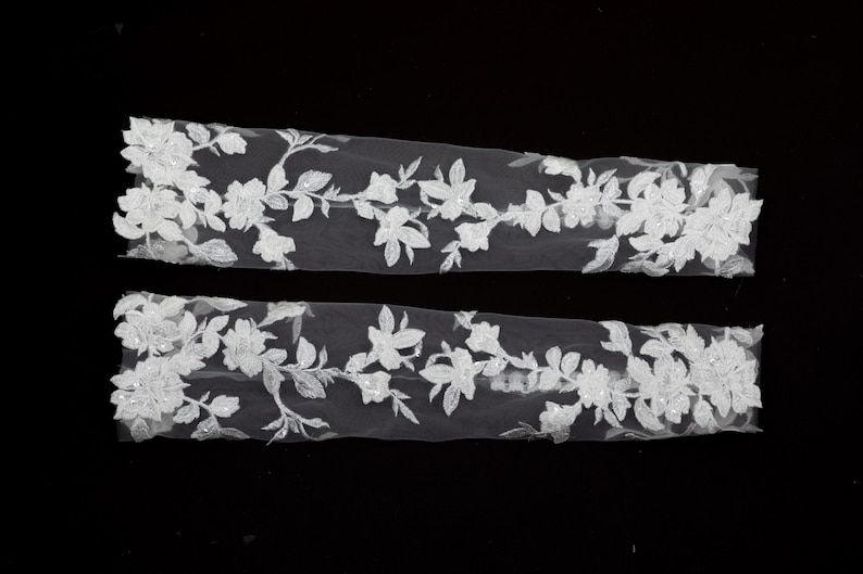 May include: Two strips of white floral lace with intricate detailing. The lace features a delicate pattern of flowers and leaves, perfect for embellishing bridal wear or other craft projects.