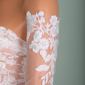 Peut inclure: Gros plan d'une manche en dentelle blanche avec broderie florale. Le design d&eacute;licat pr&eacute;sente des fleurs et des feuilles d&eacute;taill&eacute;es, cr&eacute;ant une esth&eacute;tique &eacute;l&eacute;gante et romantique. La manche est en tissu transparent, parfaite pour les mari&eacute;es ou les tenues de soir&eacute;e.