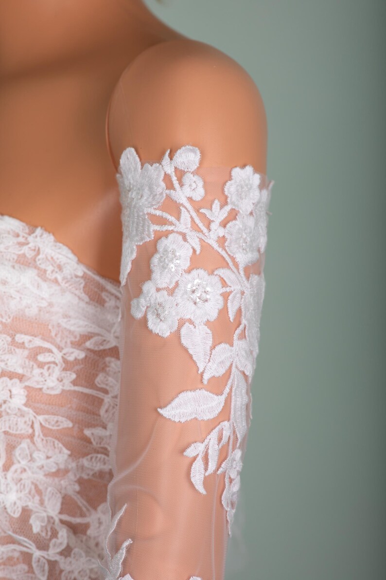Peut inclure: Gros plan d'une manche en dentelle blanche avec broderie florale. Le design d&eacute;licat pr&eacute;sente des fleurs et des feuilles d&eacute;taill&eacute;es, cr&eacute;ant une esth&eacute;tique &eacute;l&eacute;gante et romantique. La manche est en tissu transparent, parfaite pour les mari&eacute;es ou les tenues de soir&eacute;e.
