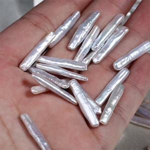 May include: A collection of white, elongated, irregular shaped pearls. The pearls are smooth and have a slight iridescent sheen.