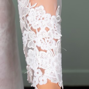 Puede incluir: Primer plano de una manga de encaje blanco. La manga presenta un intrincado bordado floral con un respaldo de malla transparente. El delicado dise&ntilde;o de encaje es detallado y elegante, lo que sugiere ropa de novia o formal.