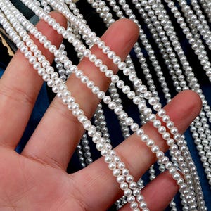 May include: A strand of white pearl beads, strung together in a long line. The beads are small and uniform in size, and they have a smooth, glossy finish.