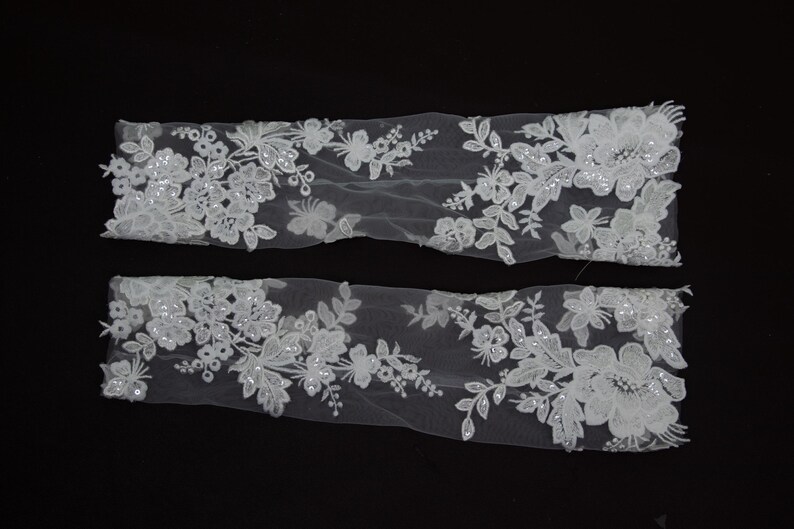Puede incluir: Dos apliques de encaje floral blanco con dise&ntilde;os intrincados. Los apliques presentan varios patrones de flores y hojas, adornados con lentejuelas. El delicado encaje se coloca sobre un fondo negro, resaltando los detalles.