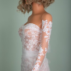 Peut inclure: Robe de mari&eacute;e blanche sans bretelles avec des d&eacute;tails de dentelle florale. La robe pr&eacute;sente un corsage ajust&eacute; et une jupe fluide. Manches longues transparentes avec de la dentelle florale assortie.