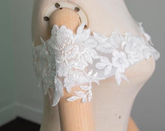 May include: White floral lace applique, with intricate flower and leaf designs. The delicate lace is displayed on a mannequin, highlighting its design and texture. Suitable for bridal wear or decorative projects.