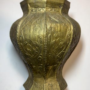 Può includere: Un vaso in metallo color ottone con forma ottagonale e corpo largo e svasato. La superficie presenta intricati motivi floreali e a farfalla in rilievo su ogni pannello, con una finitura strutturata e invecchiata su tutto l'esterno.