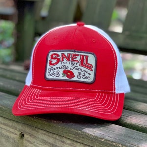 May include: Red and white trucker hat with a brown patch that says "Snell Family Farms Est. 1927" with a red flower graphic.