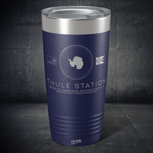 May include: A navy blue stainless steel tumbler with a white design featuring the text "THULE STATION", "ANTARCTIC NORWEGIAN RESEARCH FACILITY", and "ANTARKTISK NORSK FORSKNINGSFASTILITETER". The design also includes a white outline of Antarctica and a white flag with a red cross.