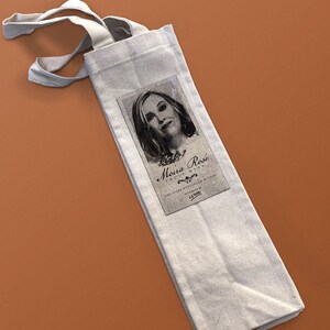 May include: A white canvas wine tote bag with a black and white label featuring a woman's portrait and the text "Moira Rosé Fruit Wine The Wine Enthusiast Winery Distributed By 55.900".