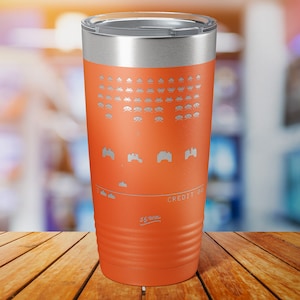 May include: Orange stainless steel tumbler with a retro video game design featuring space invaders and the text "CREDIT 00".