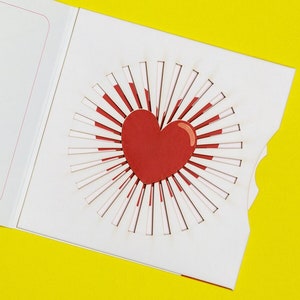 May include: A white card with a red heart pop-up design. The card is folded in half and the heart is visible when the card is open.