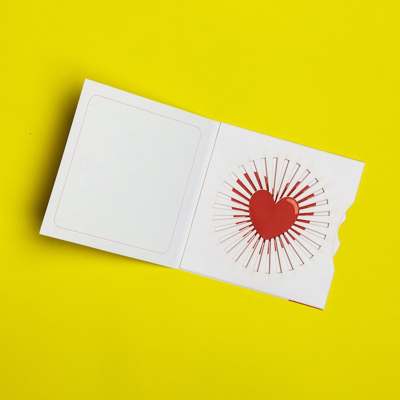 May include: A white card with a red heart pop-up design. The card is folded in half and the heart is visible when the card is open.