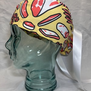 May include: A yellow surgical scrub hat with a white ribbon tie. The hat has a pattern of red and white meat cuts.