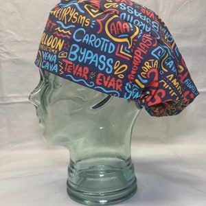 Könnte beinhalten: Eine marineblaue OP-Haube mit einem farbenfrohen Aufdruck im handschriftlichen Stil. Der Aufdruck enthält medizinische Begriffe wie "ANEURYSMS", "BYPASS" und "CAVA" in Rot-, Gelb- und Blautönen. Die Haube ist so konzipiert, dass sie auf den Kopf passt.