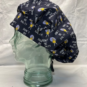 May include: A black scrub hat with a white and yellow pattern. The hat has the text "Don't Be Salty" repeated throughout the pattern.