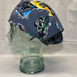 May include: A gray scrub hat with a colorful motorcycle print. The hat has a red and white trim around the edge.