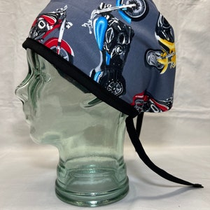 May include: A gray scrub hat with a black tie. The hat has a repeating pattern of colorful motorcycles.