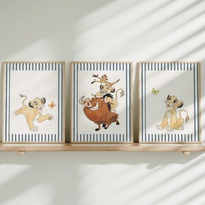 Peut inclure: Trois impressions encadrées présentant des illustrations de personnages du Roi Lion. Chaque impression a un fond blanc avec des bordures rayées bleues et blanches. Les illustrations représentent Simba, Timon, Pumbaa et un papillon.