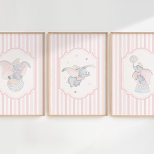 May include: Three pink and white striped prints with illustrations of Dumbo the elephant in different poses. The first print shows Dumbo holding a ball, the second shows Dumbo flying with his ears, and the third shows Dumbo standing on a pedestal.