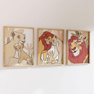 May include: Set of three framed art prints featuring illustrations of lions. The artwork depicts lion families in a cartoon style, with warm colors and a natural background. The frames are made of light-colored wood.