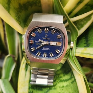 May include: A silver wristwatch with a blue face and a silver metal band. The watch face has a date window and the text "36000 ROTOMATIC" printed on it.