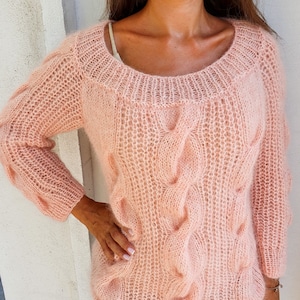 May include: A pale pink knitted jumper with a cable knit pattern. The jumper has a loose fit and long sleeves.