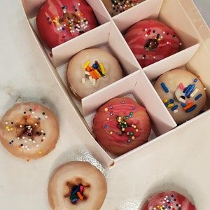 May include: A white box filled with pink and white donuts with colorful sprinkles. The donuts are arranged in rows and columns. There are also three donuts outside of the box.