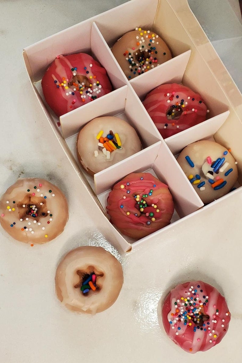 May include: A white box filled with pink and white donuts with colorful sprinkles. The donuts are arranged in rows and columns. There are also three donuts outside of the box.