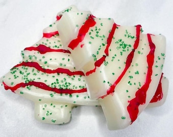 Puede incluir: Un jabón blanco con forma de árbol de Navidad con rayas rojas y chispas verdes. El jabón tiene un diseño festivo, perfecto para regalos navideños o decoración de temporada. El jabón no está perfumado.