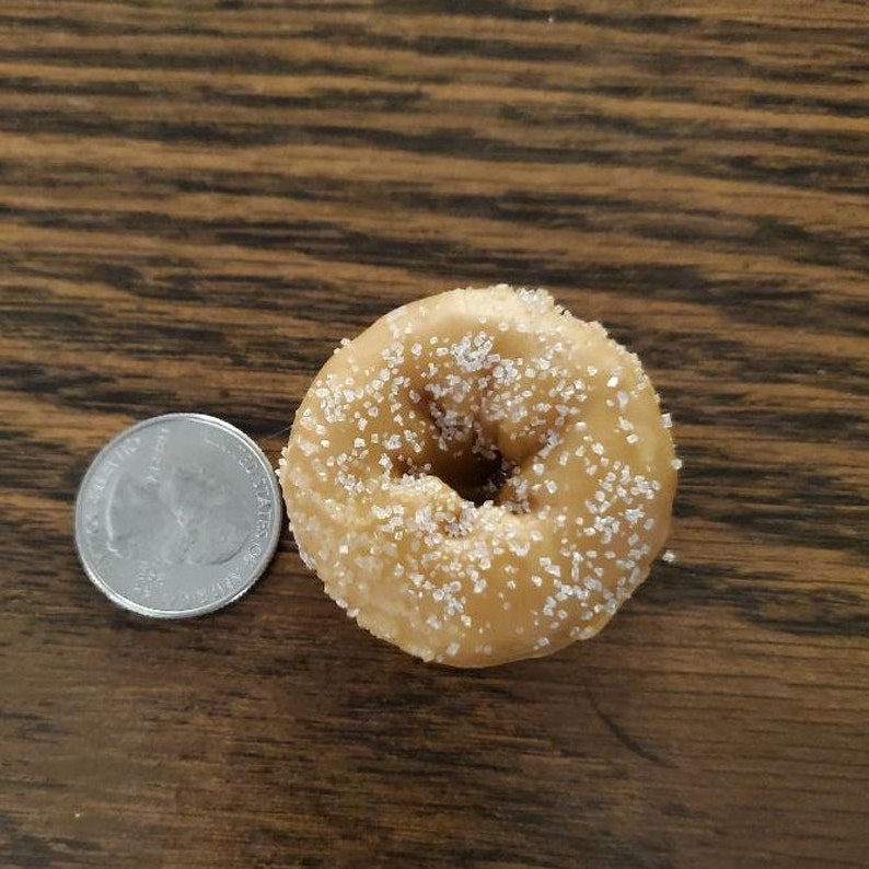 May include: A single, round, sugar-coated donut with a hole in the center. The donut is light brown and has a white sugar coating.