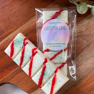 May include: A white wax melt bar with red and green accents. The bar is labeled "Northern Chic's Christmas Cakes" and "Handmade in Ohio Wax Melt, Net Wt (1.75 oz)".