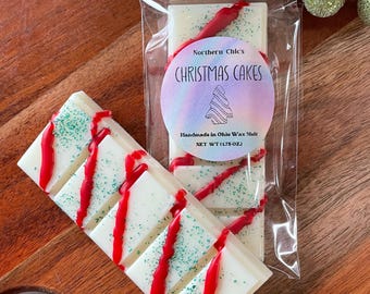 May include: A white wax melt bar with red and green accents. The bar is labeled "Northern Chic's Christmas Cakes" and "Handmade in Ohio Wax Melt, Net Wt (1.75 oz)".