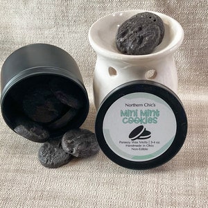 May include: A black tin filled with small, dark gray wax melts labeled "Northern Chic's Mini Mint Cookies" with the text "Parasoy Wax Melts | 3-4 oz. Handmade in Ohio Non-Edible".