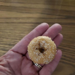 May include: A small, round donut with a hole in the center, covered in white sugar sprinkles.