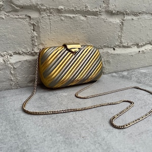 Op de afbeelding: Een gouden en zilveren gestreepte clutch met een kettingband.