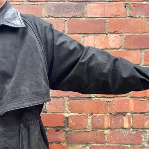 May include: A black leather jacket with a drawstring waist and a collar. The jacket is shown against a brick wall.