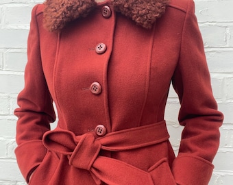 Puede incluir: Abrigo de lana rojo con cuello de piel sintética marrón. El abrigo tiene cinturón en la cintura, botones y mangas largas. Un abrigo de estilo clásico, adecuado para el clima frío.