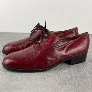 May include: A pair of burgundy leather dress shoes. The shoes have a classic design with a lace-up closure, rounded toe, and a low heel. The shoes are in good condition and appear to be vintage.