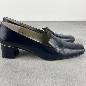 May include: A pair of navy blue leather heeled loafers. The shoes have a square toe, a block heel, and a gold accent on the heel. The shoes are size 39, with a 5 cm heel.