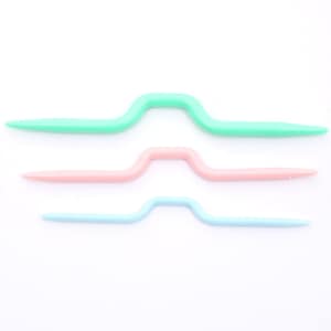 May include: Three plastic crochet hooks in different colours: light green, pink, and light blue. The hooks are arranged in a row, with the largest hook at the top and the smallest hook at the bottom.