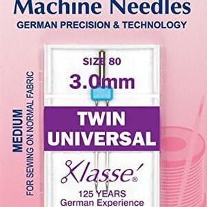 May include: A pack of one Hemline Klasse Twin Universal sewing machine needles, size 80, 3.0 mm, for medium weight fabrics. The packaging is pink and white with the Hemline logo and the words "German Precision & Technology" and "125 Years German Experience".