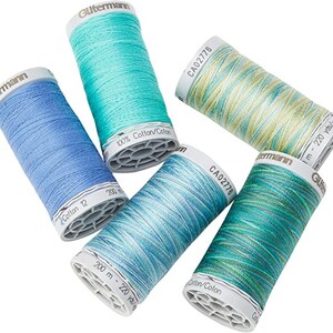 May include: Five spools of Gutermann thread in various shades of blue and green. The spools are labelled with the brand name, thread type, and length in metres and yards. The thread is 100% cotton.