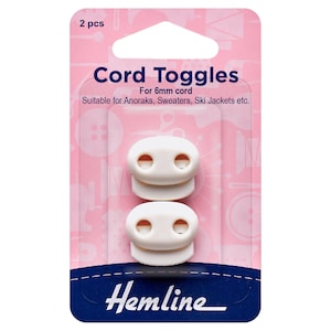 May include: Two white plastic cord toggles for 6mm cord. The toggles are packaged on a pink and blue card with the text "Cord Toggles" and "Hemline".