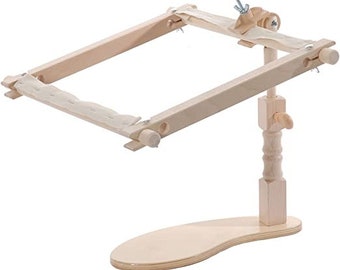 May include: A wooden embroidery hoop stand with a natural finish. The stand has a base with a curved shape and a vertical post that supports the hoop. The hoop is adjustable and can be tilted to different angles.