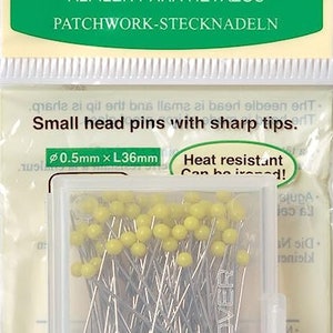 May include: A clear plastic container filled with a large quantity of small head sewing pins with yellow and blue coloured heads. The pins are 0.5mm in diameter and 36mm long. The container is labelled "Clover" and the text "Heat resistant! Can be ironed!" is printed on the container.