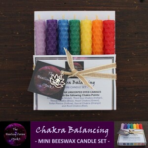 May include: A set of seven mini beeswax candles in a rainbow of colours, packaged in a small box with a brown ribbon. The candles are labelled "Chakra Balancing - Mini Beeswax Candle Set -" and are associated with the seven chakras.